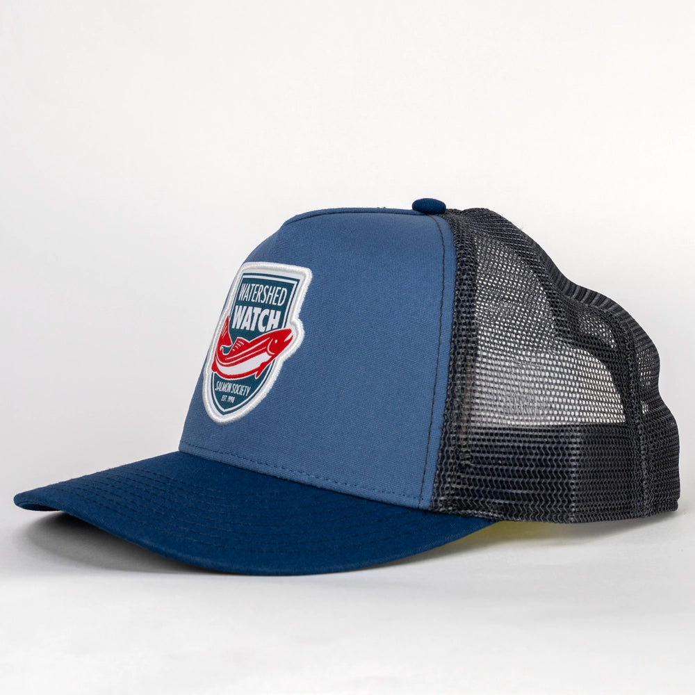 A Dusk Blue / Navy trucker hat with a black mesh back, featuring a 'Watershed Watch' logo patch on the front panel.